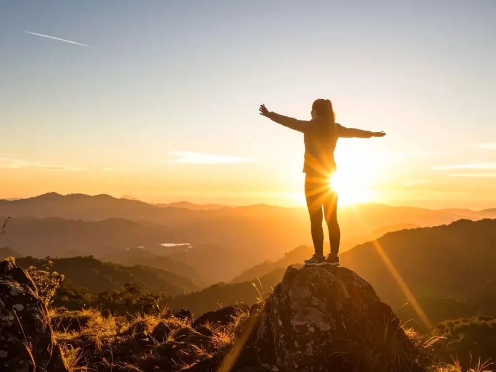 Mensch breitet Arme aus auf einem Berggipfel bei Sonnenaufgang – Symbol für Lebensfreude und volles Leben