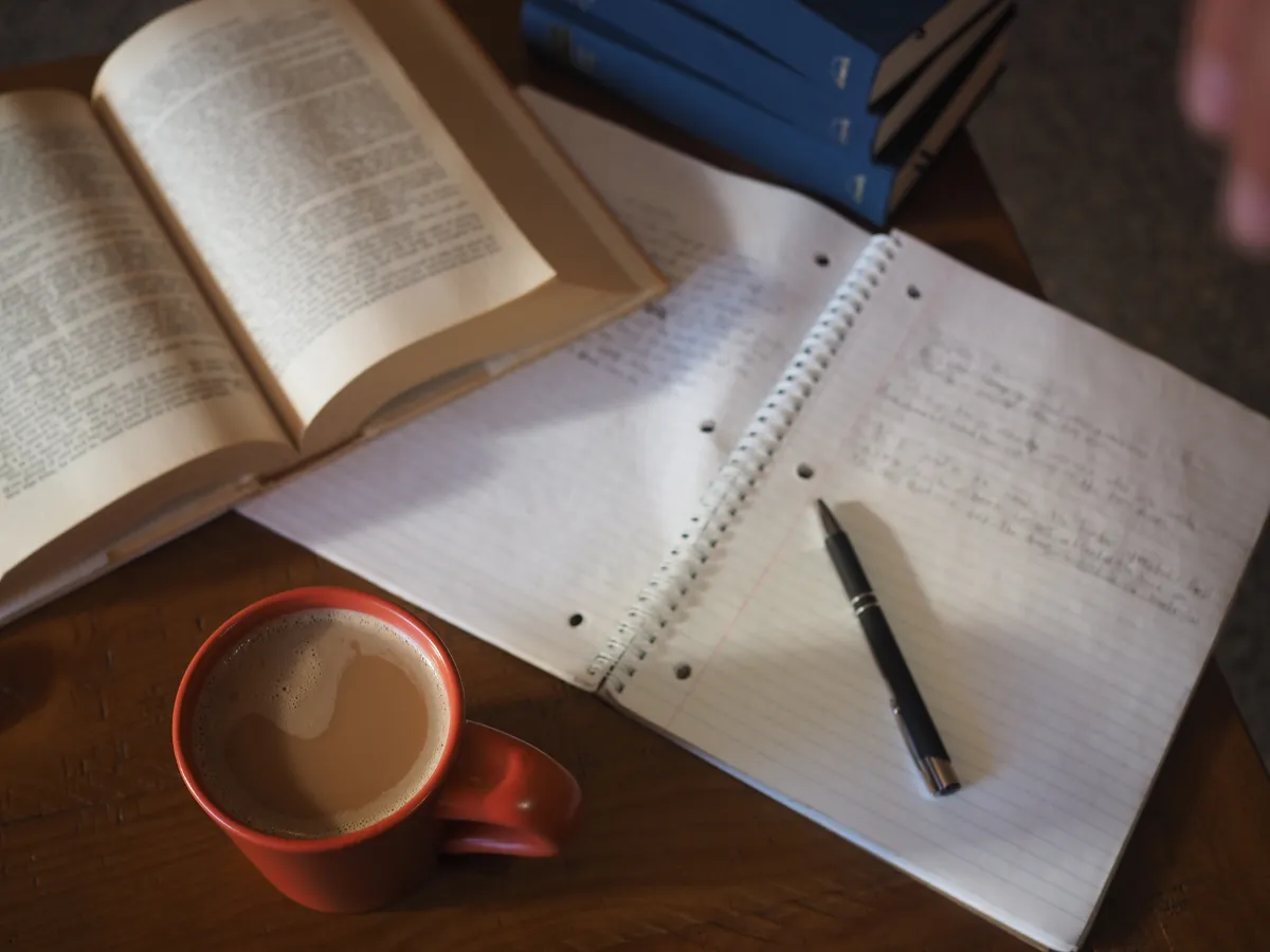 Notizbuch mit handschriftlichen Gedanken, daneben eine Tasse Kaffee – Symbol für stilles Lernen und Offenheit.