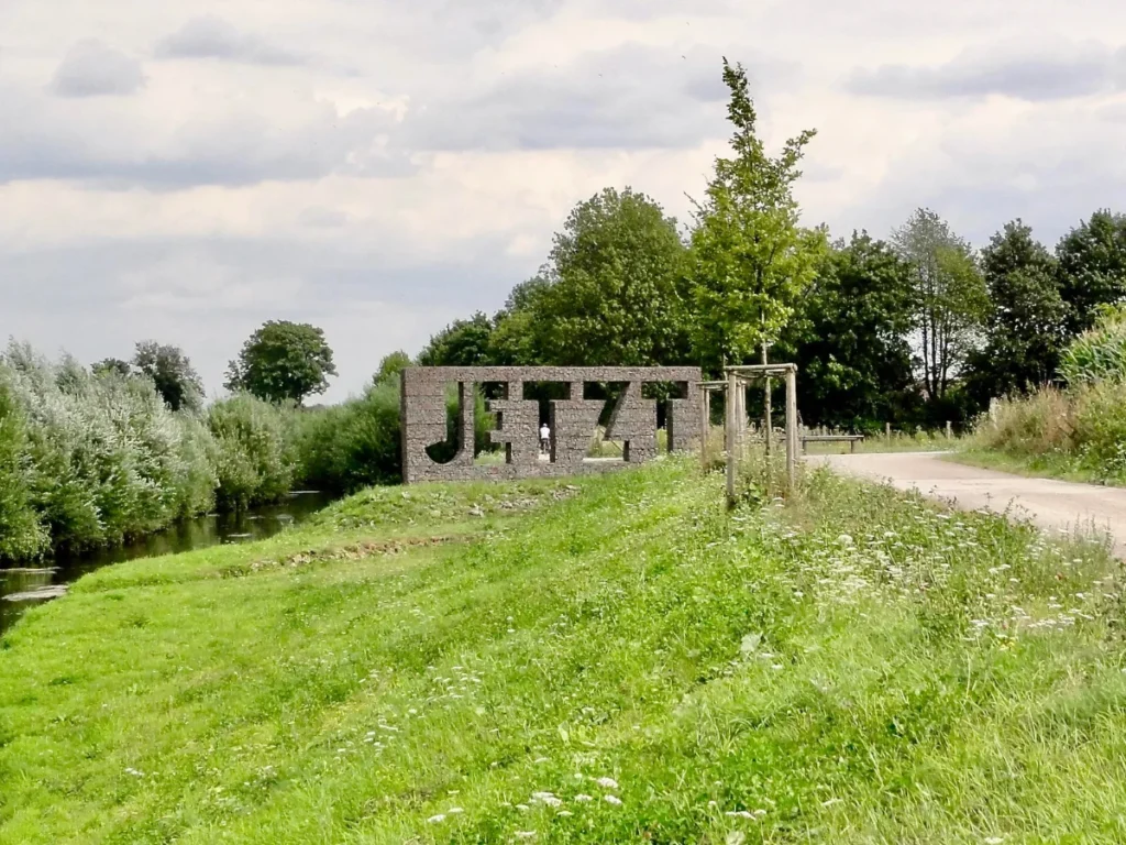 Große Steinskulptur mit dem Schriftzug „JETZT“ in einer ruhigen Landschaft – Symbol für Präsenz und Augenblick.