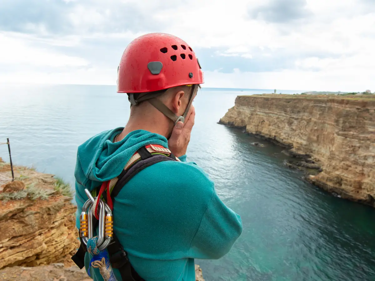 Person mit Kletterausrüstung blickt nachdenklich über eine Klippe auf das Meer – Sinnbild für mentale Grenzen und den Sprung ins Unbekannte.