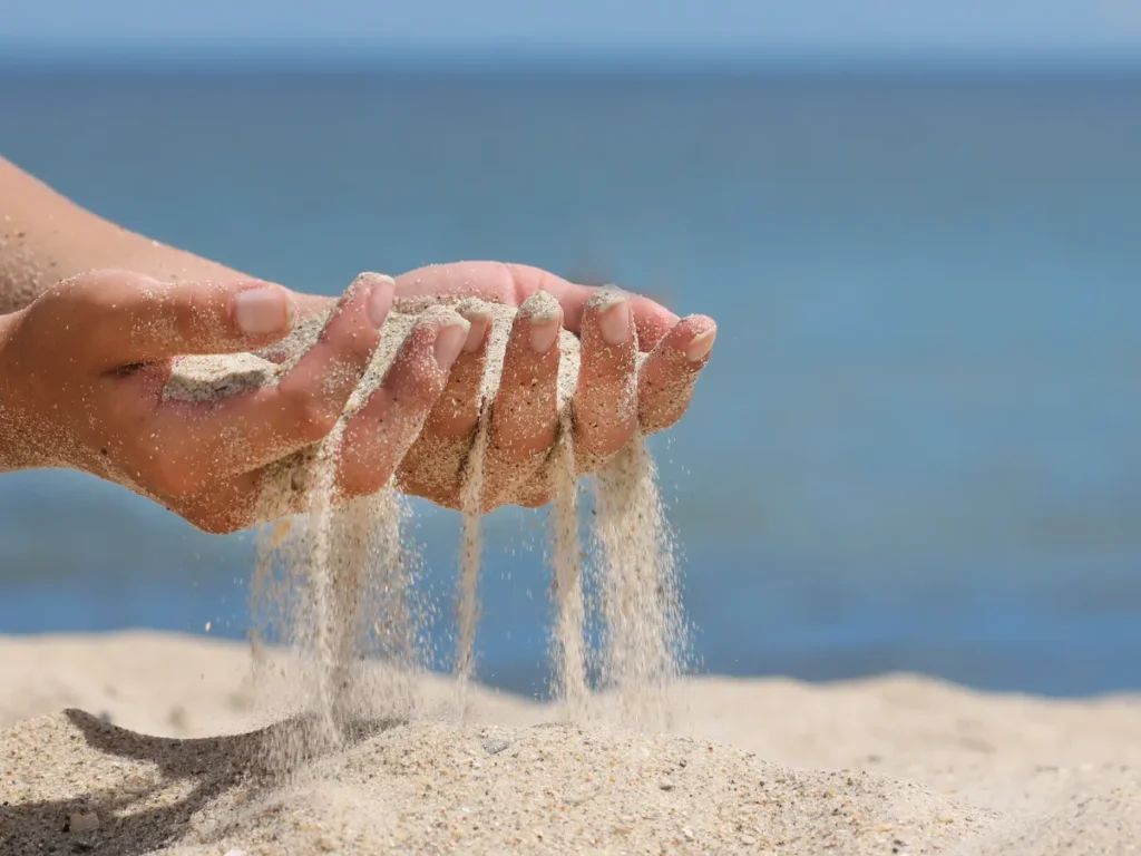 Hände lassen Sand in den Wind fallen – Sinnbild für Loslassen von Ärger und das Öffnen für Positives