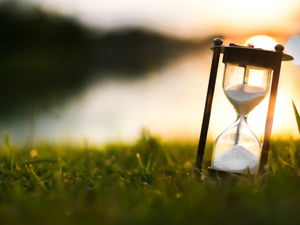 Sanduhr im Sonnenuntergang auf einer Wiese – Symbol für die Vergänglichkeit der Zeit und die Bedeutung, den jetzigen Moment bewusst zu leben.