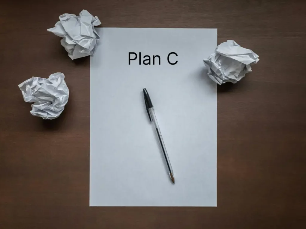 Leeres Blatt mit der Aufschrift „Plan C“, umgeben von zerknülltem Papier und einem Kugelschreiber – Symbol für neue Lösungsansätze nach gescheiterten Versuchen.