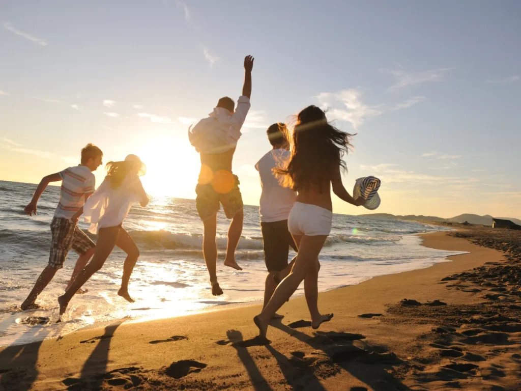Gruppe junger Menschen springt lachend am Strand entlang in der Abendsonne – Symbol für Fröhlichkeit, Lebensfreude und unbeschwerte Gemeinschaft.