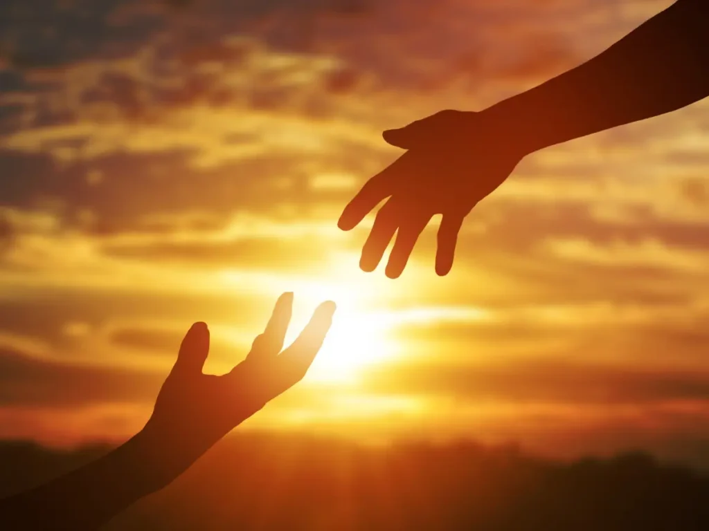 Zwei sich entgegenstreckende Hände vor einem warmen Sonnenuntergang – Symbol für Verbundenheit, Unterstützung und Zuversicht.